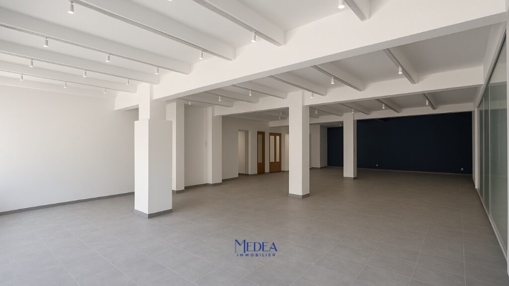 Grand espace lumineux avec piliers, murs blancs et sol carrelé gris