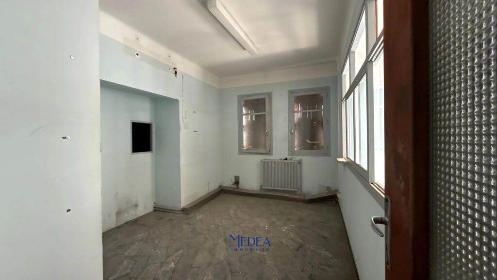 Bureau vide avec des murs bleus pâles, deux fenêtres et un radiateur