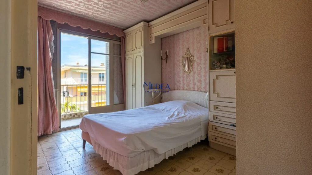 Chambre avec lit, armoire et balcon donnant sur un bâtiment